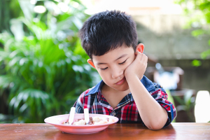 Asian little boy boring eating with rice food on the wooden table